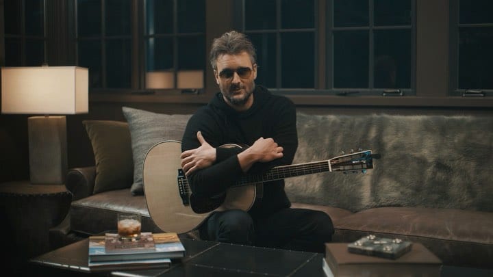 Eric Church sitting on a couch holding a guitar