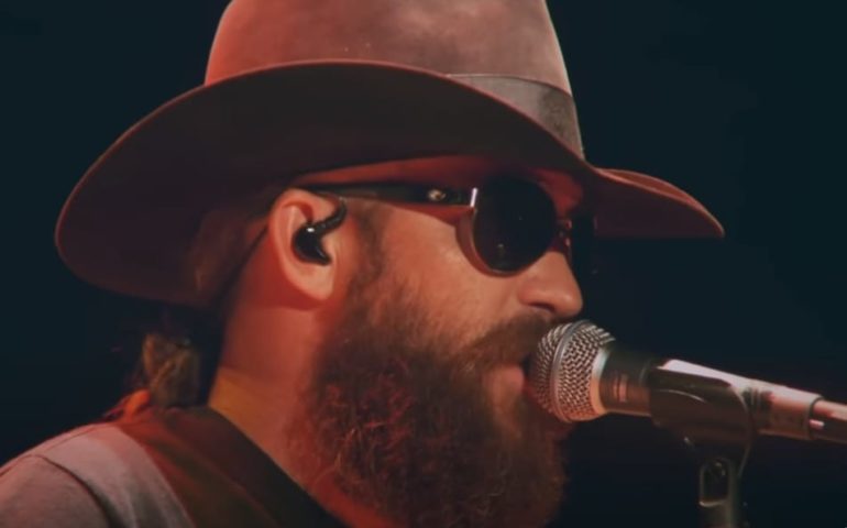 A man wearing a hat and sunglasses singing into a microphone