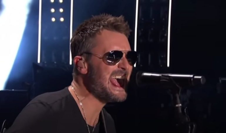 A man with a beard and wearing glasses singing into a microphone