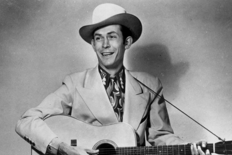 Hank Williams in a suit and tie playing a guitar