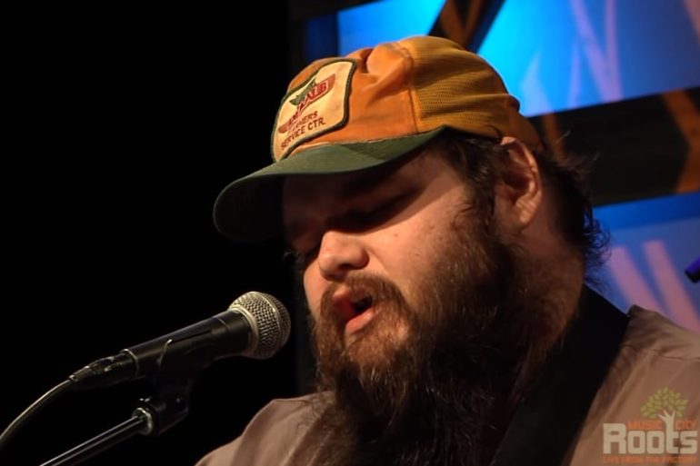 A man with a beard and a hat with a microphone in front of him