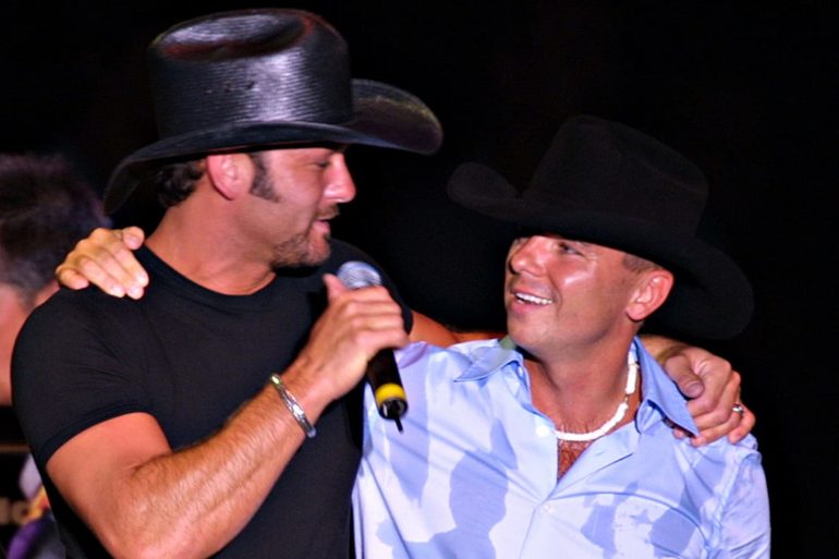 A man singing into a microphone next to a man wearing a hat