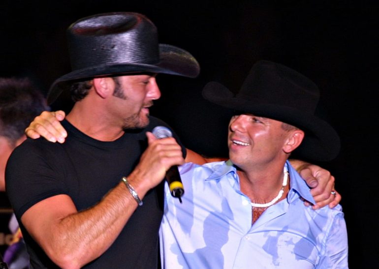 A man singing into a microphone next to a man wearing a hat