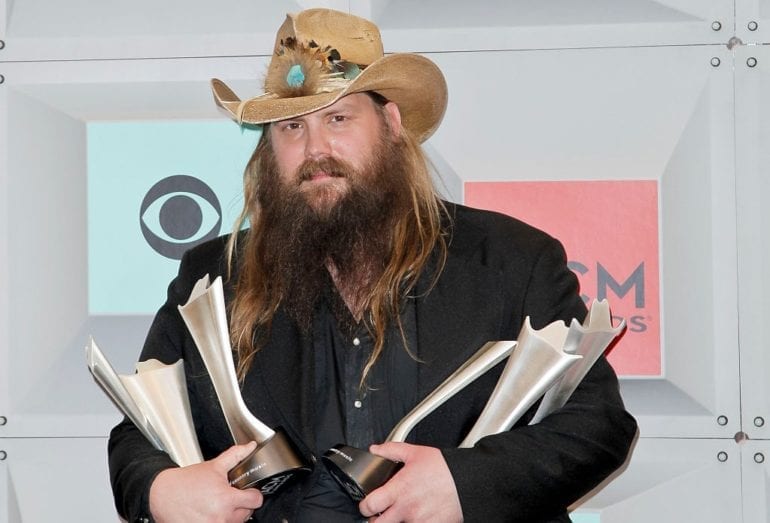 Chris Stapleton with a hat and a beard holding a gun