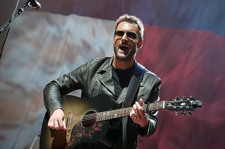 Eric Church with a beard and sunglasses playing a guitar