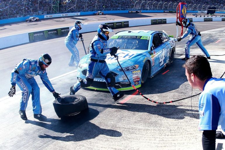 A group of people in blue jumpsuits with a car on a track