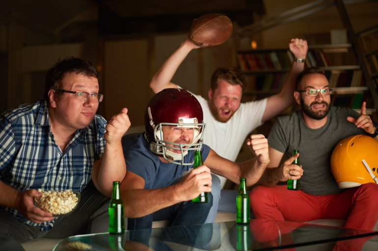 A group of men sitting at a table with beer bottles and a football