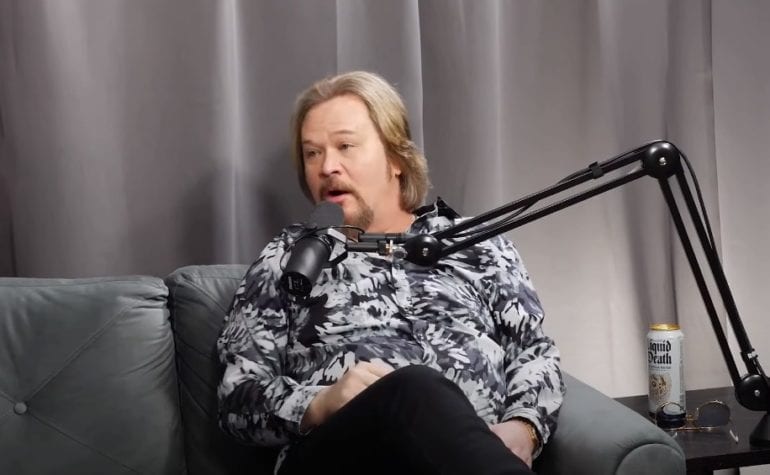 Travis Tritt sitting on a couch with a microphone