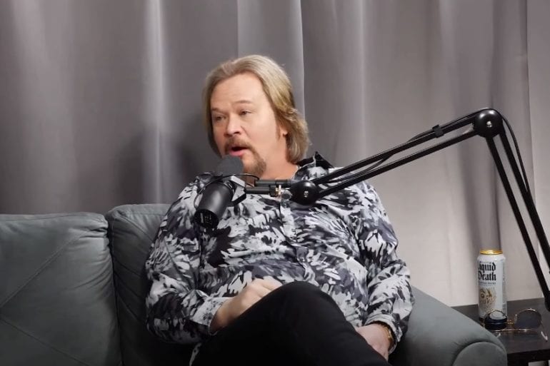 Travis Tritt sitting on a couch with a microphone