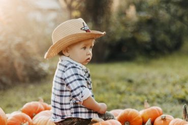 A baby wearing a hat sitting in a pile of pumpkins