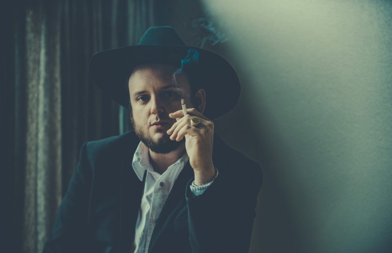 A man in a suit and hat smoking a cigarette