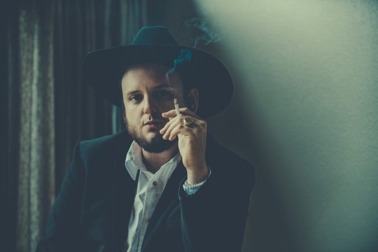 A man in a suit and hat smoking a cigarette