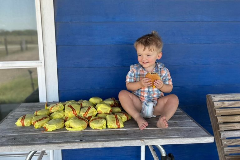 A boy sitting on a bench with a pile of bananas
