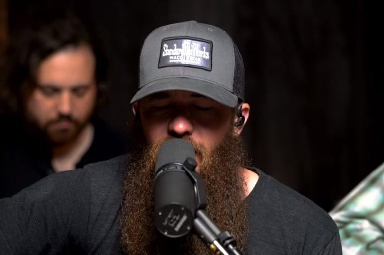 A man with a beard and a hat holding a microphone