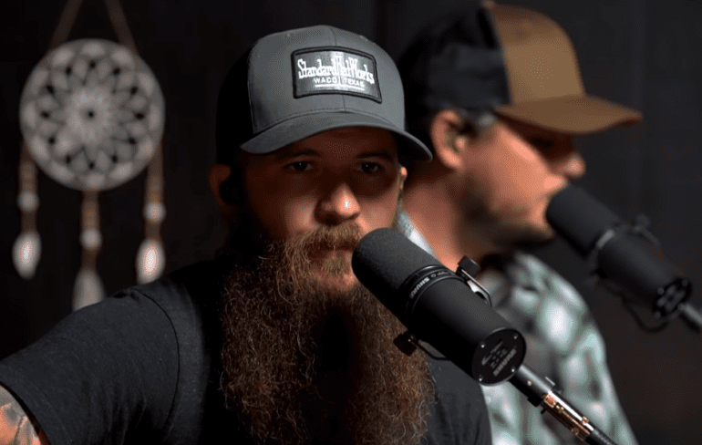 A man with a beard and a hat with a microphone in front of him