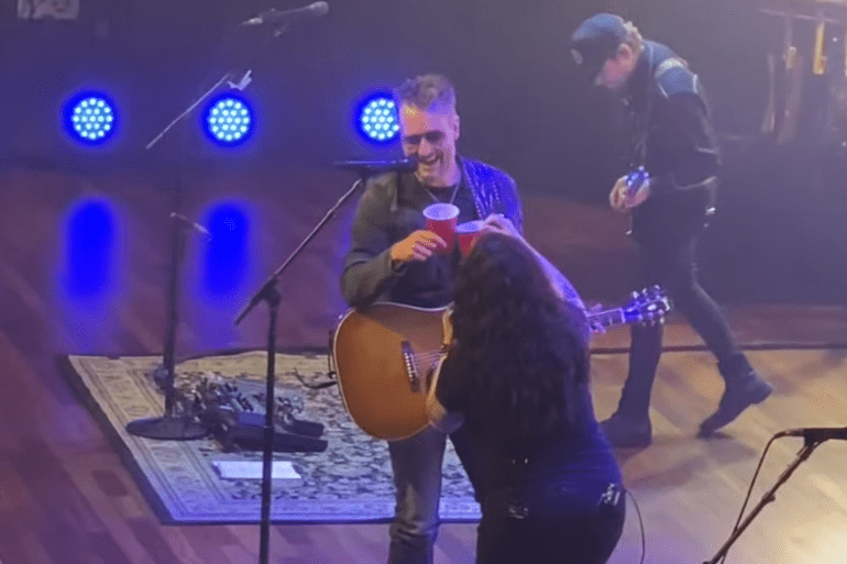 A man singing into a microphone on a stage with a woman holding a microphone and a guitar and