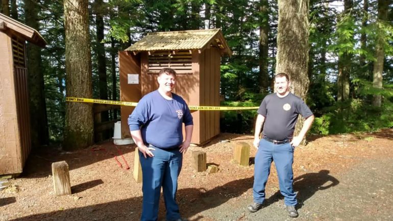 Two men standing in front of a wooden structure in a forest