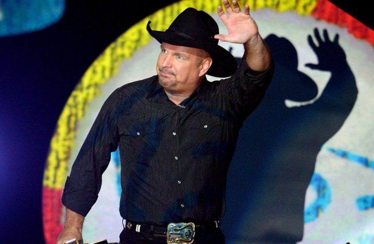 Garth Brooks wearing a hat and holding his hand up
