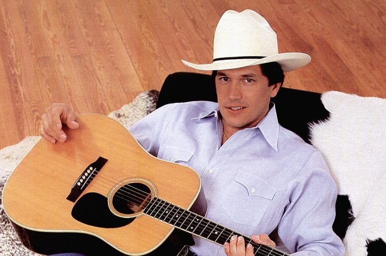 George Strait sitting on a couch with a guitar