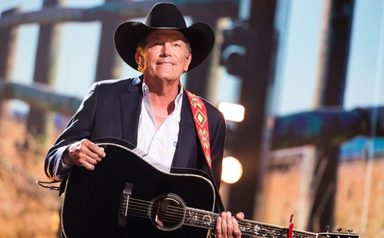George Strait in a hat and a black jacket playing a guitar