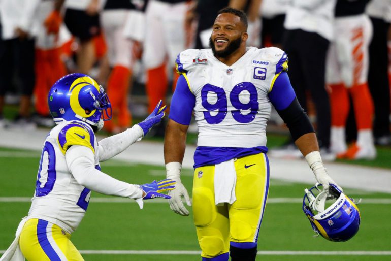 Aaron Donald in a blue uniform with a blue helmet and a white shirt with a blue and yellow
