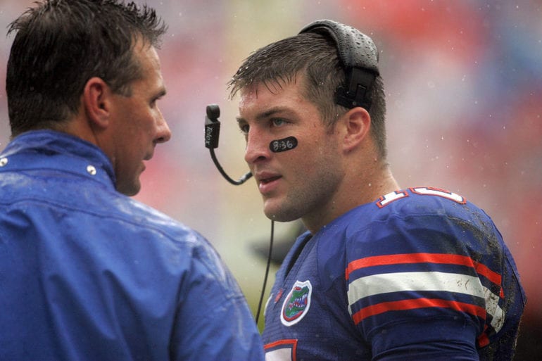 Tim Tebow in a blue shirt talking to a man in a blue uniform