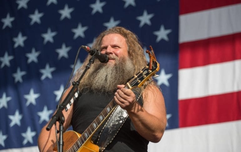 Jamey Johnson playing a guitar in front of a flag
