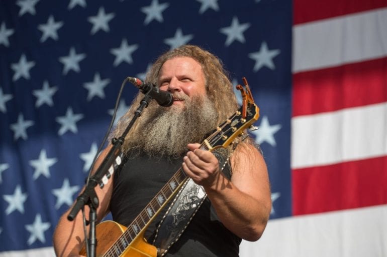 Jamey Johnson playing a guitar in front of a flag