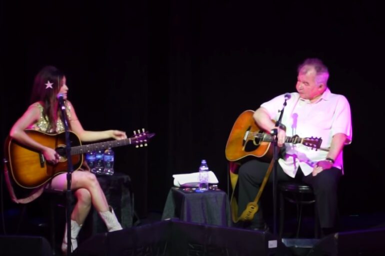 A man and woman playing guitars on a stage