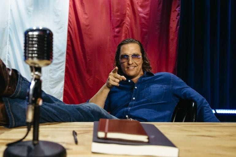Matthew McConaughey sitting at a desk with a microphone and a box