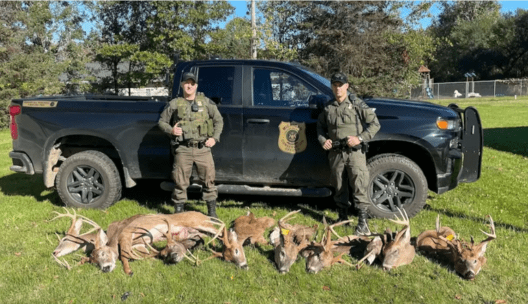 A couple of men in military uniforms with deer in front of a truck