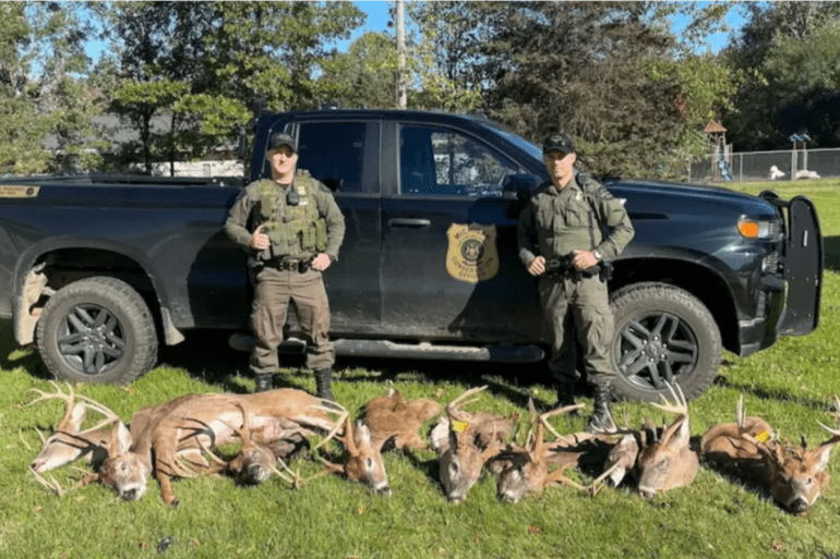 A couple of men in military uniforms with deer in front of a truck