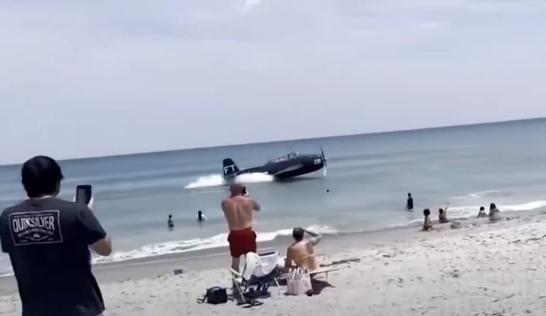 A man taking a picture of a plane on a beach
