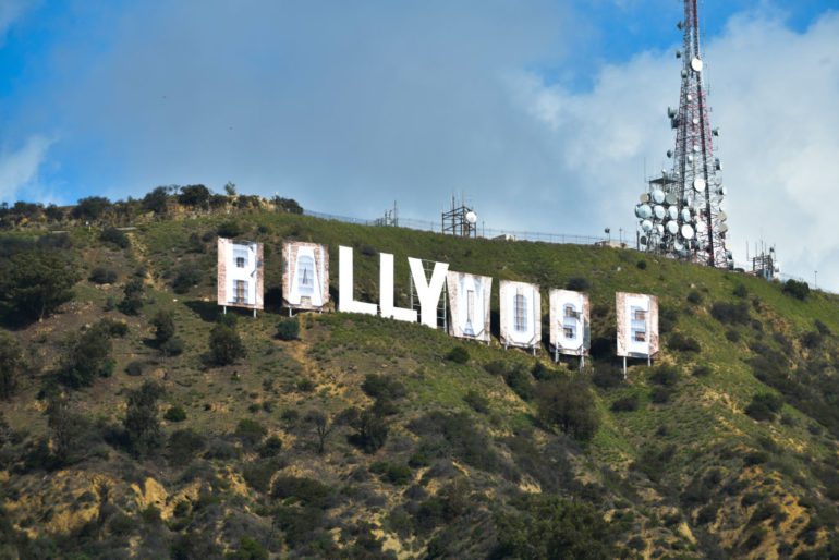 A group of white structures on a hill with Hollywood Sign in the background