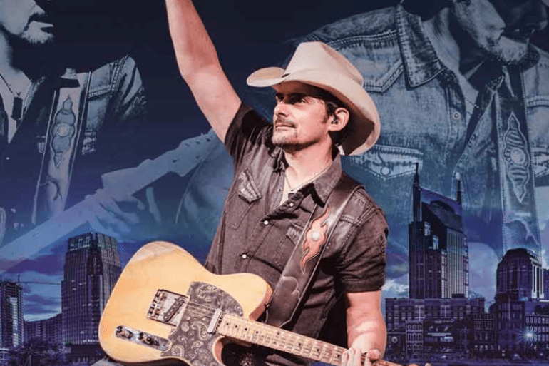 Brad Paisley with a hat and a guitar in front of a large mural