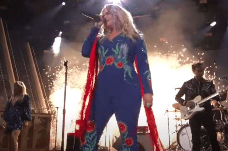 A woman with long hair and a red and blue costume playing a guitar on a stage with a