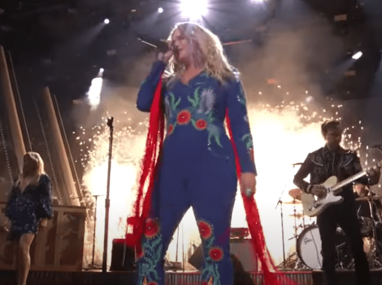 A woman with long hair and a red and blue costume playing a guitar on a stage with a