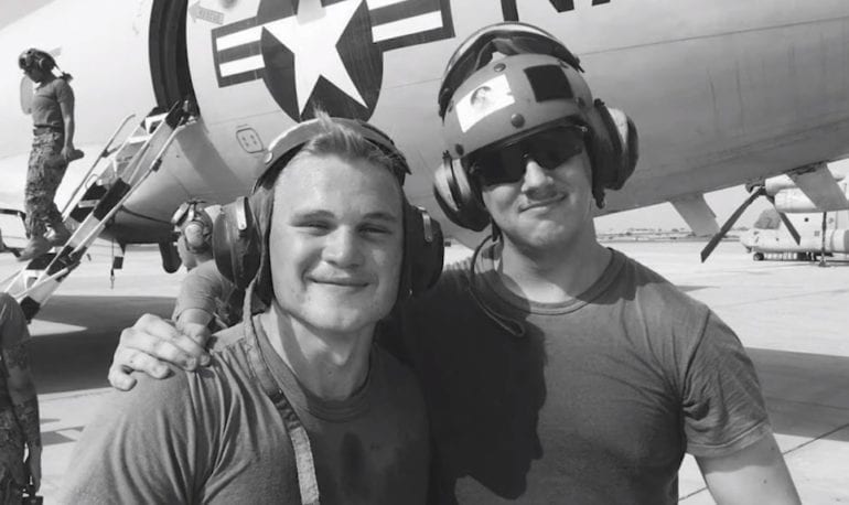 A couple of men posing for a picture next to a plane