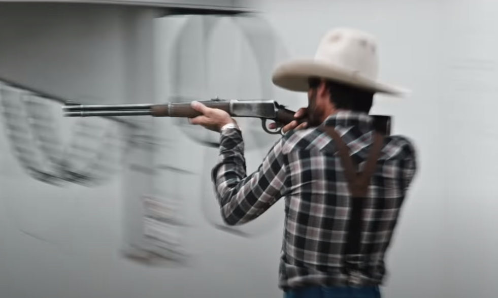 A man in a cowboy hat aiming a rifle