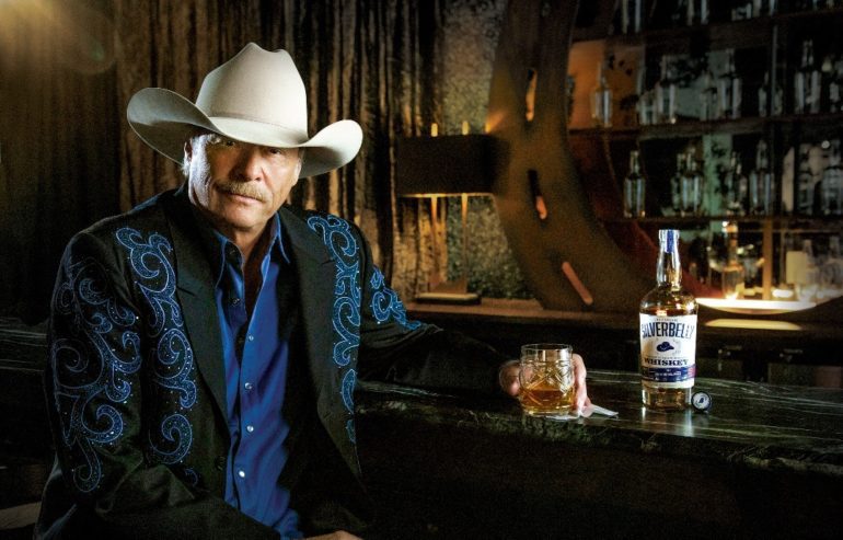 Alan Jackson country musicd sitting at a table with a bottle of alcohol